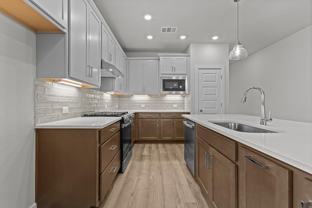 kitchen with stainless steel appliances, sink, pendant lighting, white cabinets, and light hardwood / wood-style floors