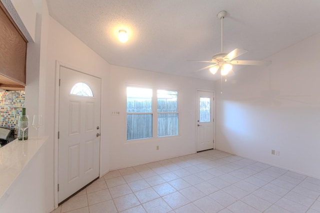 foyer entrance featuring light tile patterned flooring, ceiling fan, vaulted ceiling, and a textured ceiling