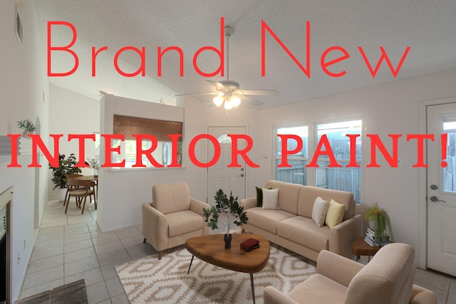 tiled living room with ceiling fan, vaulted ceiling, and a textured ceiling