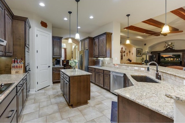 kitchen with light stone countertops, a kitchen island, pendant lighting, and appliances with stainless steel finishes