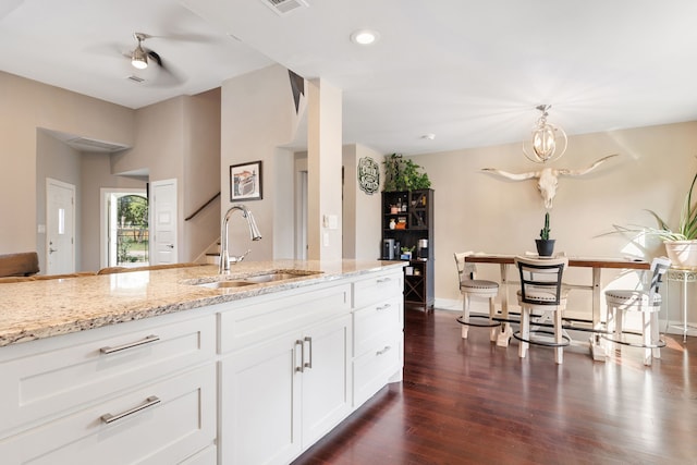 kitchen featuring dark hardwood / wood-style floors, decorative light fixtures, white cabinetry, sink, and light stone countertops