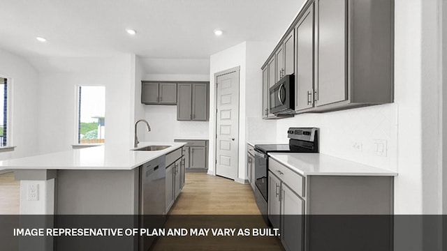 kitchen with appliances with stainless steel finishes, an island with sink, sink, light wood-type flooring, and gray cabinetry