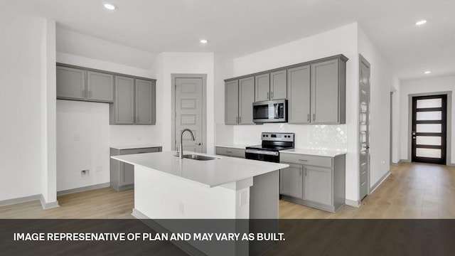 kitchen featuring an island with sink, appliances with stainless steel finishes, sink, and gray cabinets