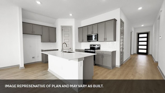 kitchen with stainless steel appliances, gray cabinetry, a kitchen island with sink, light hardwood / wood-style flooring, and sink