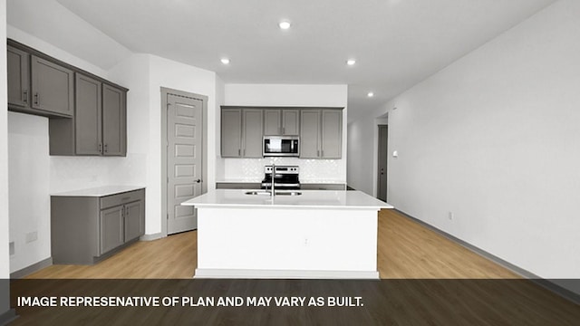 kitchen featuring stainless steel appliances, light hardwood / wood-style floors, a center island with sink, and gray cabinets