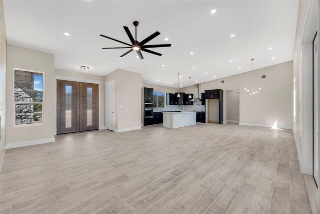 unfurnished living room with sink, light hardwood / wood-style flooring, and ceiling fan with notable chandelier