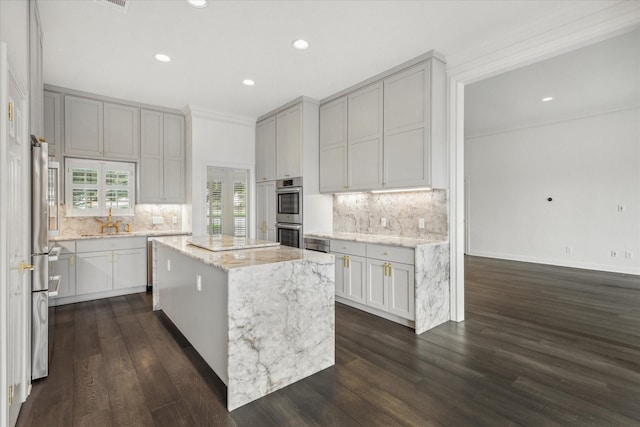 kitchen with light stone countertops, sink, a kitchen island, ornamental molding, and stainless steel appliances