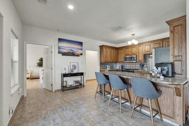 kitchen with light stone counters, brown cabinets, stainless steel appliances, tasteful backsplash, and a peninsula