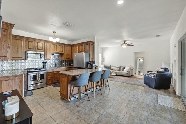 kitchen with brown cabinetry, a breakfast bar area, stainless steel appliances, and open floor plan