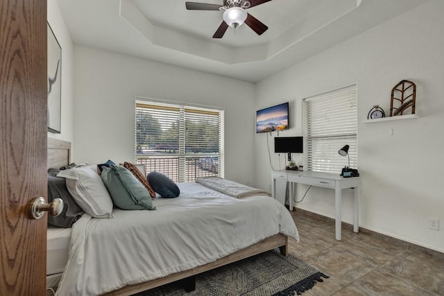 bedroom with a tray ceiling, a ceiling fan, and baseboards