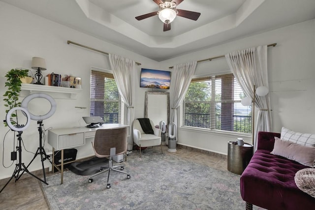 home office with a ceiling fan, a tray ceiling, and baseboards