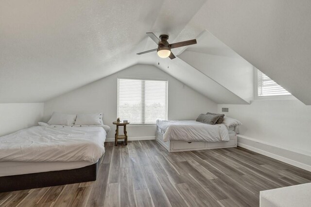 bedroom with vaulted ceiling, ceiling fan, a textured ceiling, wood finished floors, and baseboards
