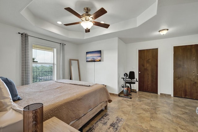 bedroom with a tray ceiling, ceiling fan, and baseboards
