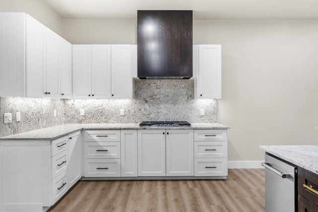 kitchen featuring light stone counters, backsplash, range hood, and white cabinets