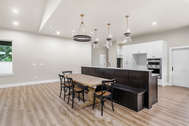 kitchen featuring light hardwood / wood-style flooring, pendant lighting, stainless steel double oven, a large island, and white cabinets