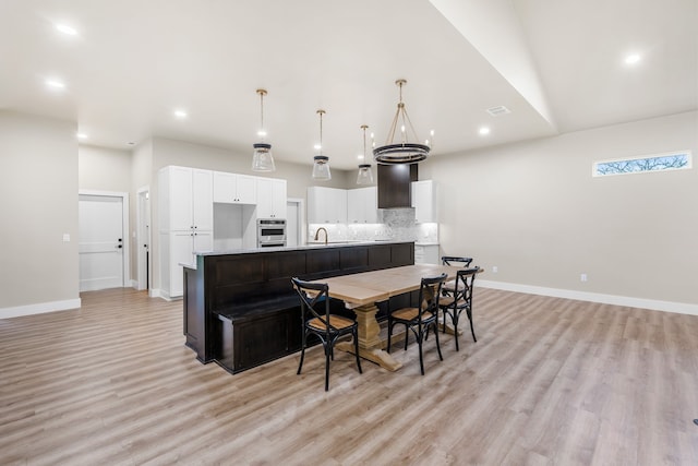 kitchen featuring sink, white cabinetry, light wood-type flooring, an island with sink, and pendant lighting