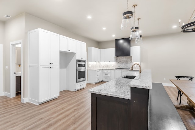 kitchen featuring wall chimney exhaust hood, sink, white cabinetry, hanging light fixtures, and decorative backsplash