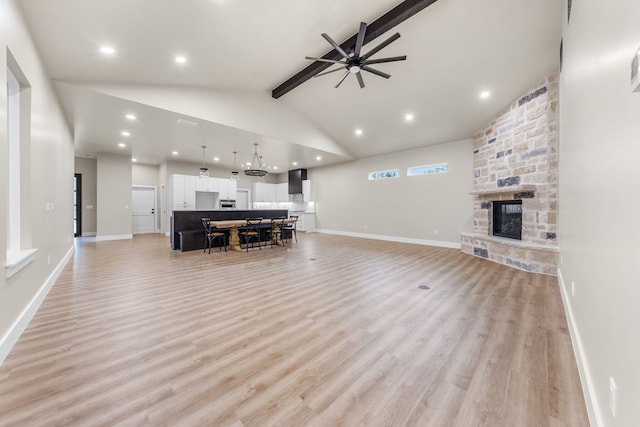 living room featuring ceiling fan, high vaulted ceiling, light hardwood / wood-style floors, a stone fireplace, and beamed ceiling