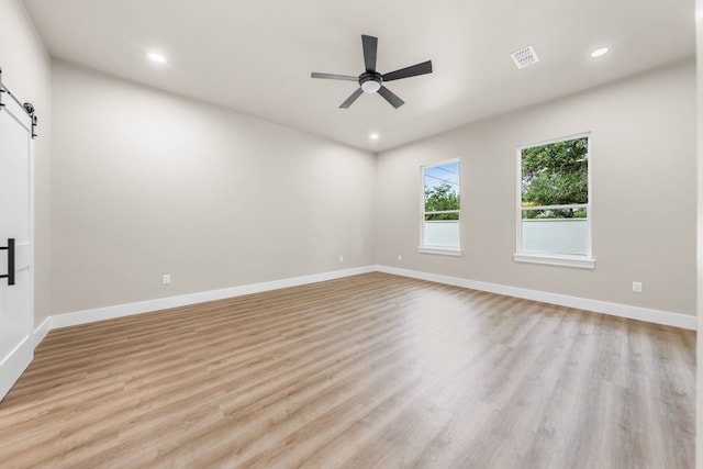 empty room with ceiling fan, a barn door, and light hardwood / wood-style floors