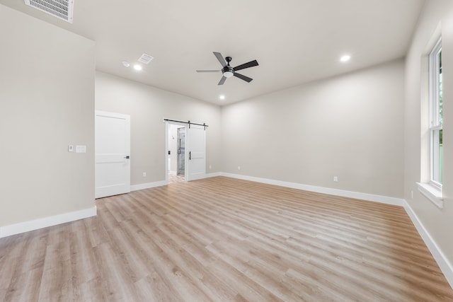 empty room featuring light hardwood / wood-style flooring, a barn door, and ceiling fan