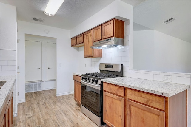 kitchen featuring stainless steel gas range, light stone counters, a textured ceiling, decorative backsplash, and light wood-type flooring