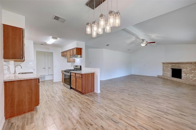 kitchen featuring sink, stainless steel gas range, a fireplace, decorative light fixtures, and light wood-type flooring