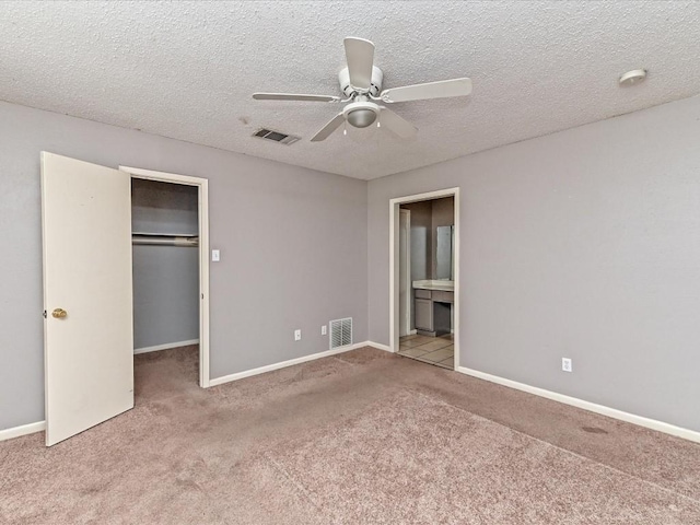 unfurnished bedroom with a walk in closet, light colored carpet, a textured ceiling, and a closet