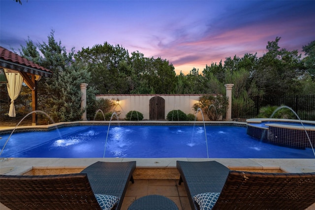 pool at dusk featuring an in ground hot tub and pool water feature