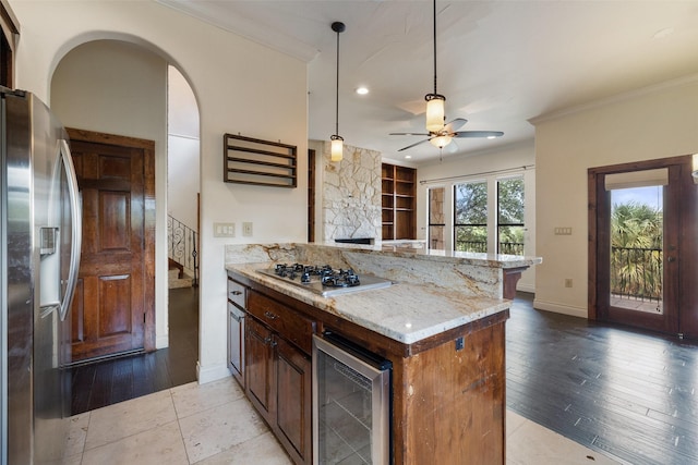 kitchen with light stone countertops, appliances with stainless steel finishes, wine cooler, ornamental molding, and kitchen peninsula