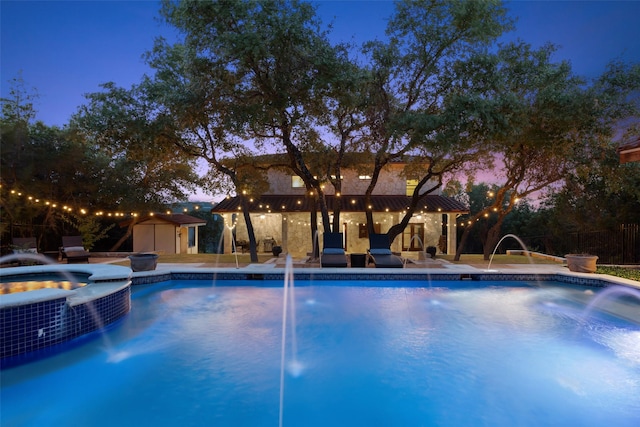 pool at dusk with an in ground hot tub, pool water feature, and a storage shed