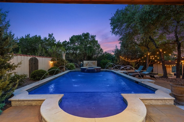 pool at dusk featuring an in ground hot tub, a patio area, and pool water feature