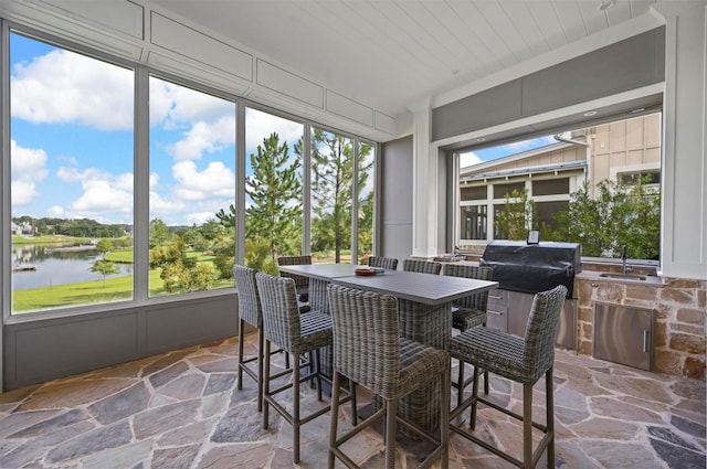 sunroom / solarium with wood ceiling, sink, and a water view