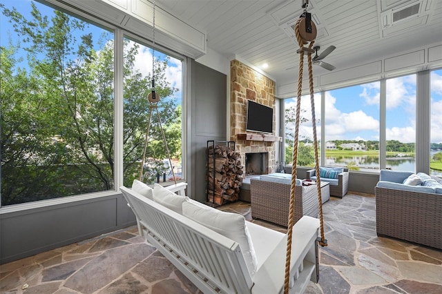 sunroom with ceiling fan, a healthy amount of sunlight, and a stone fireplace