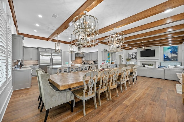 dining space with an inviting chandelier, beamed ceiling, and light wood-type flooring