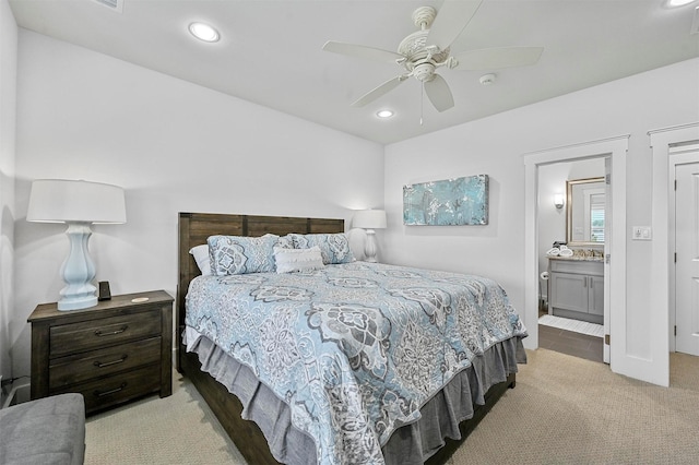 bedroom with ceiling fan, light colored carpet, and ensuite bath