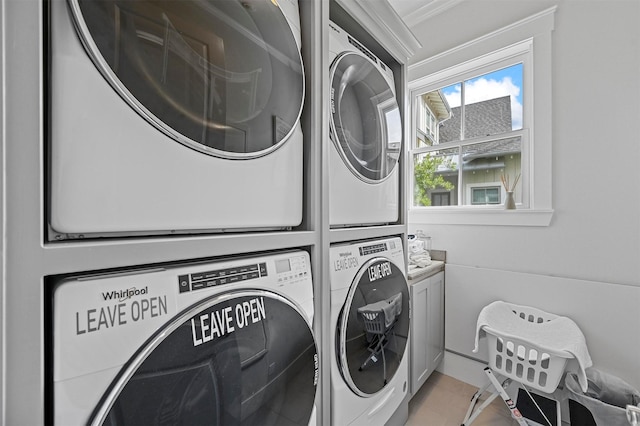 clothes washing area with stacked washer and dryer, cabinets, ornamental molding, and light tile patterned floors