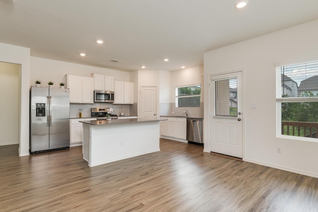 kitchen featuring hardwood / wood-style flooring, backsplash, white cabinets, a center island, and stainless steel appliances