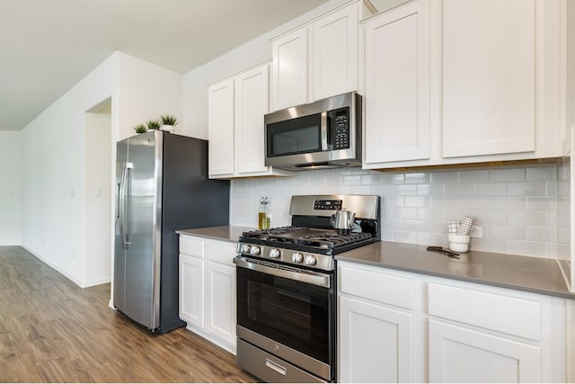 kitchen featuring stainless steel appliances, white cabinetry, decorative backsplash, and wood-type flooring