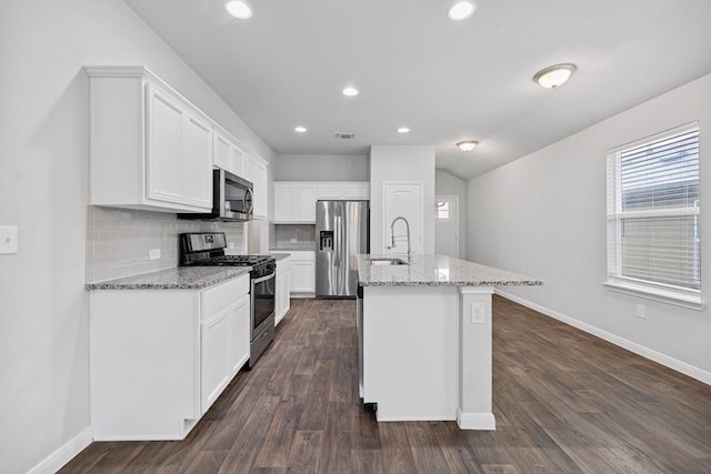 kitchen featuring an island with sink, light stone countertops, appliances with stainless steel finishes, white cabinets, and decorative backsplash