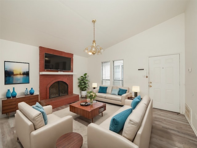 living room featuring a notable chandelier, light hardwood / wood-style flooring, a brick fireplace, and high vaulted ceiling