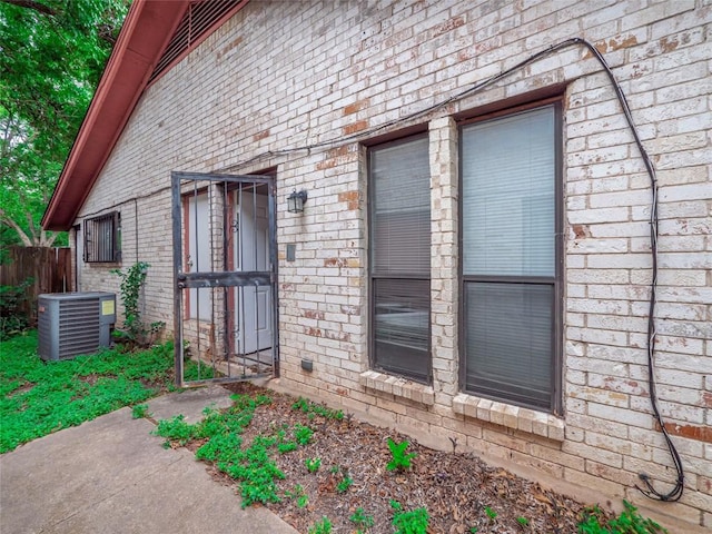 view of exterior entry featuring brick siding, central AC unit, and fence