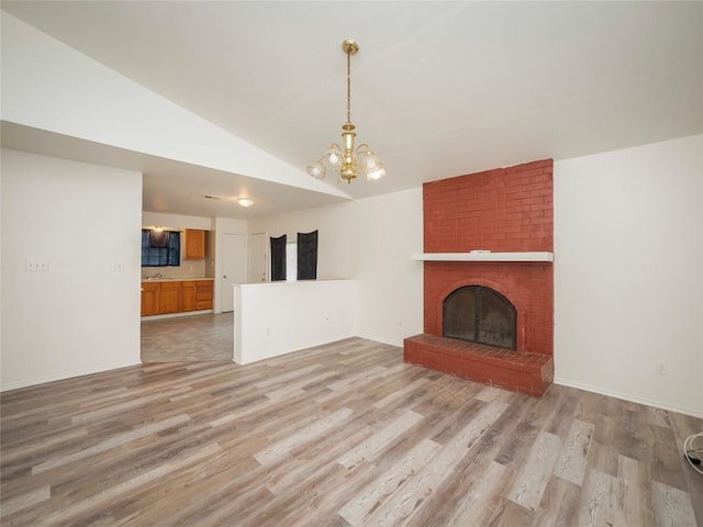 unfurnished living room with light wood finished floors, an inviting chandelier, a fireplace, and lofted ceiling