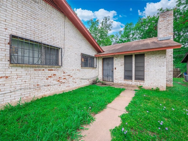 doorway to property featuring a yard, brick siding, cooling unit, and a chimney