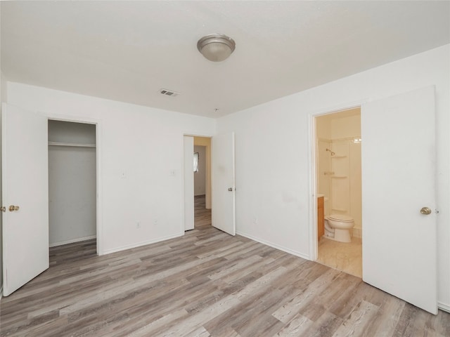 unfurnished bedroom featuring ensuite bath, a closet, and hardwood / wood-style floors