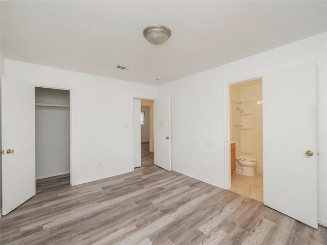 unfurnished bedroom with wood finished floors, visible vents, baseboards, ensuite bath, and a closet