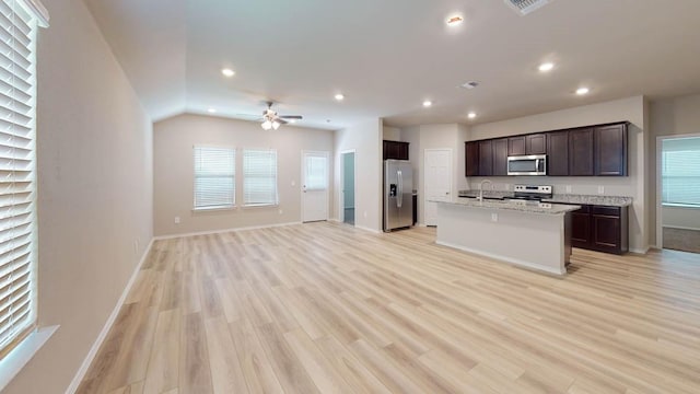 kitchen with sink, appliances with stainless steel finishes, light stone counters, an island with sink, and light wood-type flooring