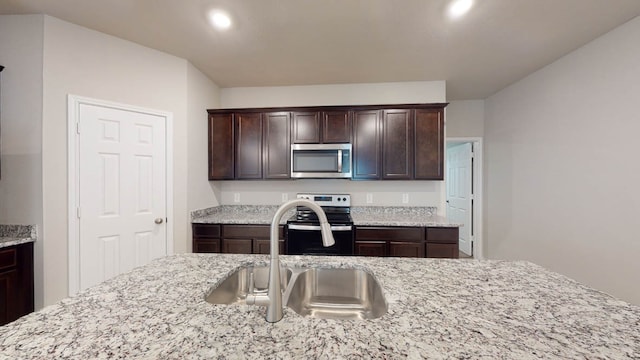 kitchen with appliances with stainless steel finishes, dark brown cabinetry, sink, and light stone countertops