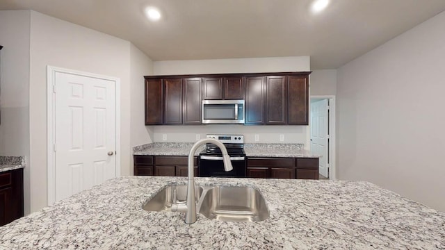 kitchen featuring dark brown cabinetry, stainless steel appliances, light stone countertops, and sink