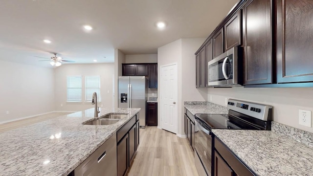 kitchen with dark brown cabinetry, sink, light stone counters, stainless steel appliances, and light hardwood / wood-style floors