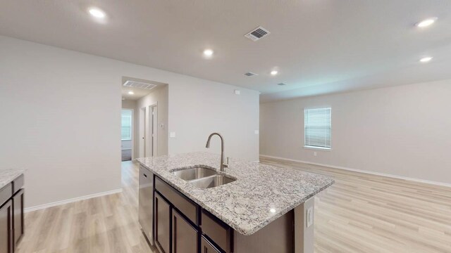 kitchen with light stone counters, an island with sink, sink, stainless steel dishwasher, and light hardwood / wood-style flooring